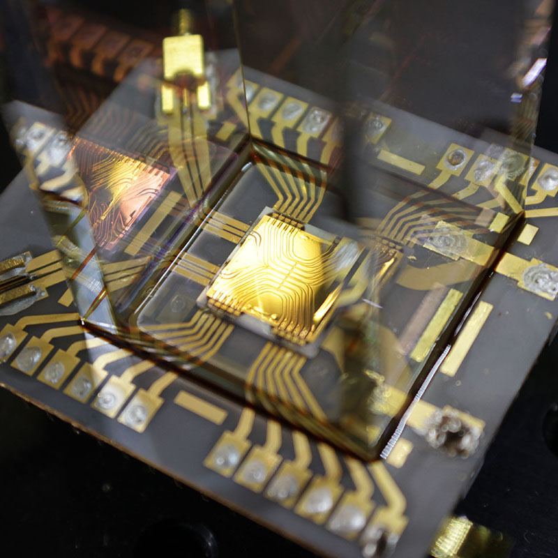 Close-up of a microchip mounted on a circuit board with gold conductive pathways and electronic connections.