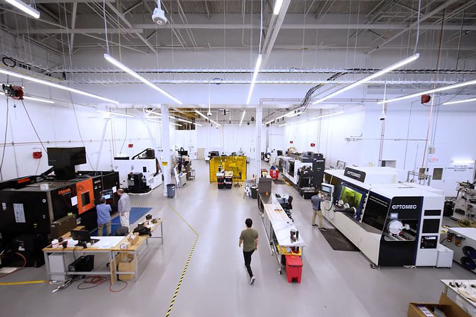 High-angle view of an advanced manufacturing facility with large industrial fabrication and machining systems, workstations, and personnel operating equipment on the production floor.