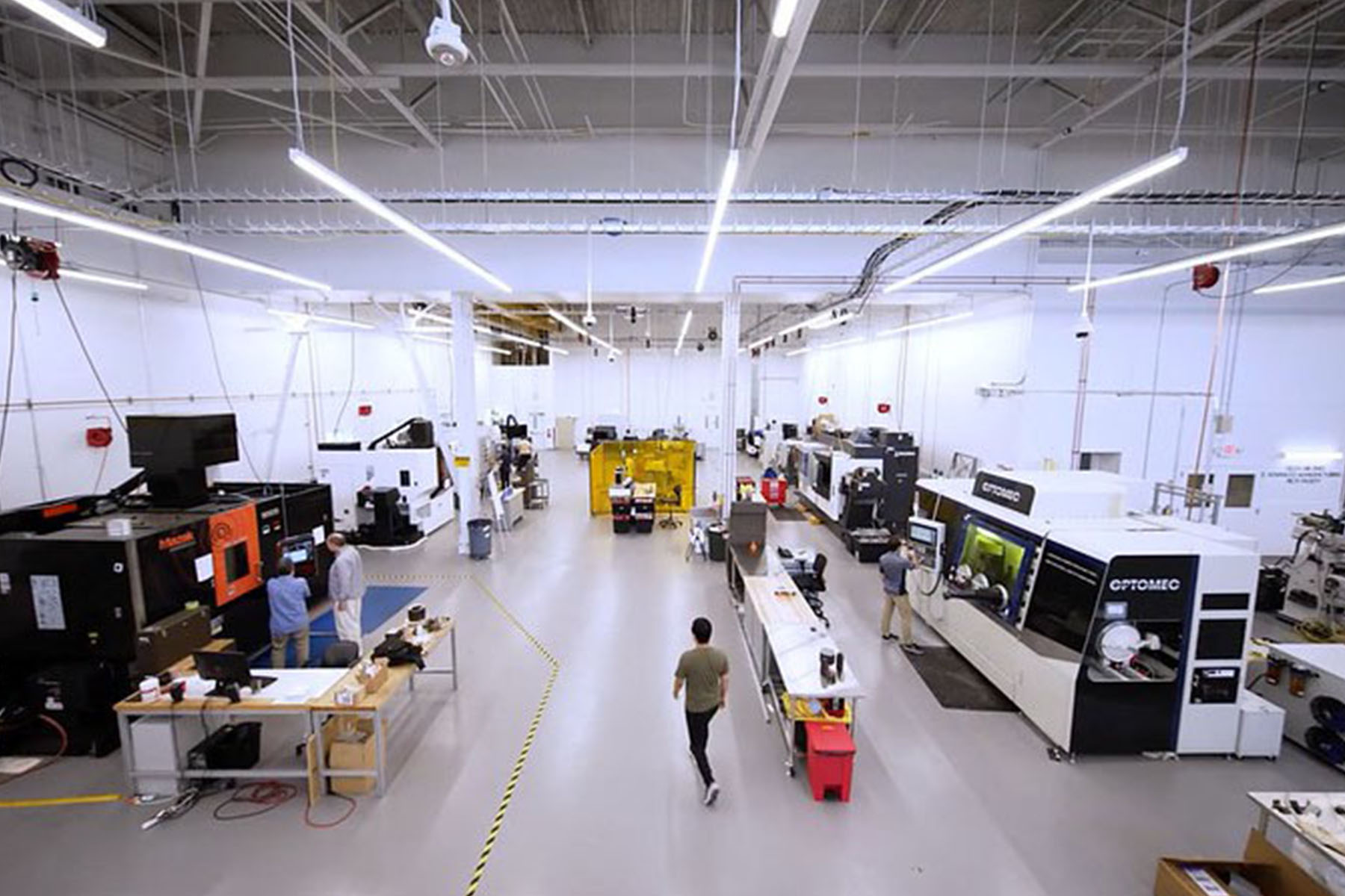 High-angle view of an advanced manufacturing facility with large industrial fabrication and machining systems, workstations, and personnel operating equipment on the production floor.