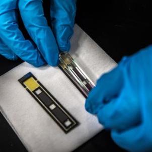 A person wearing blue protective gloves handles components of an atomic magnetometer on a white cloth in a laboratory setting.