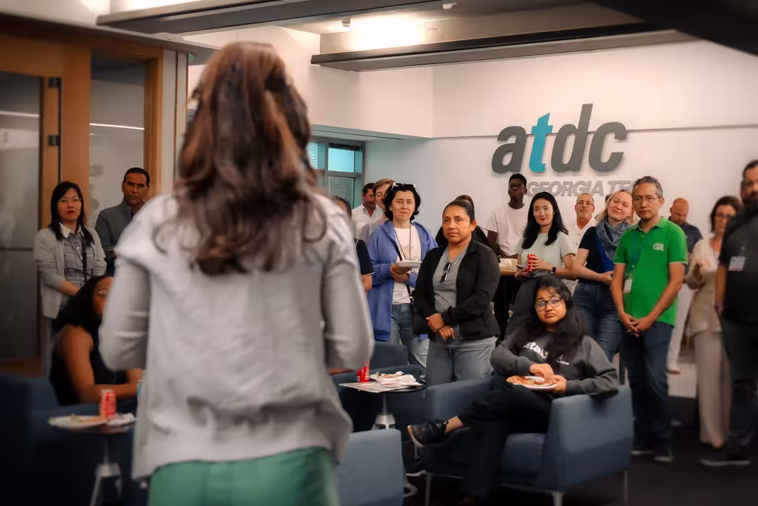 Speaker addresses a gathering of attendees in the ATDC Georgia Tech office while participants listen and socialize.