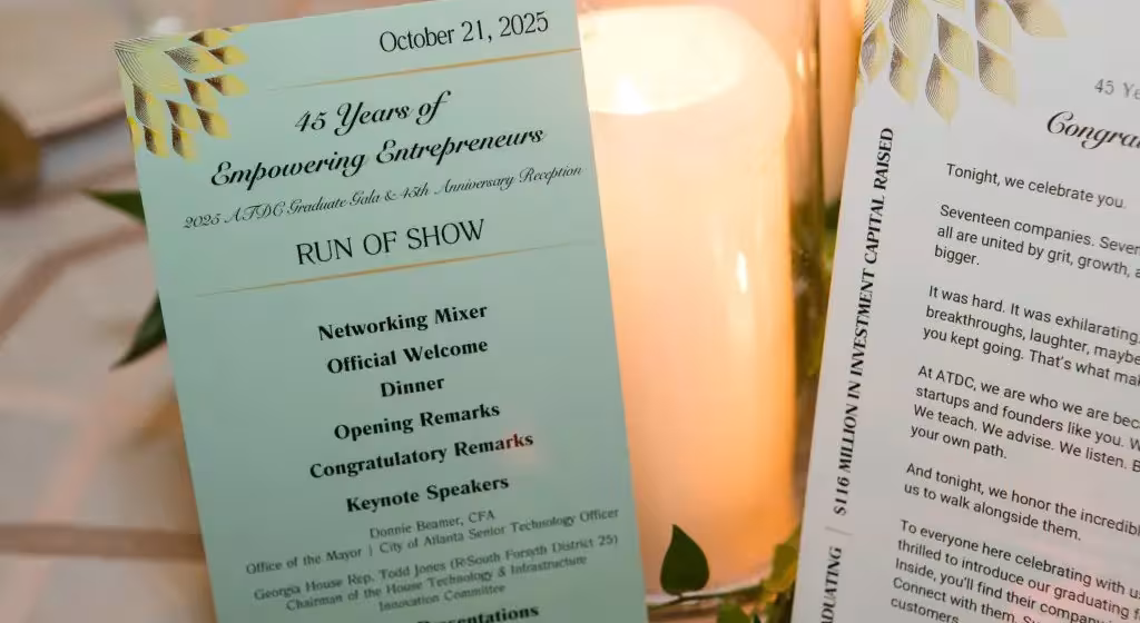 ATDC anniversary event program displayed beside a candle, listing the evening's schedule and speakers.