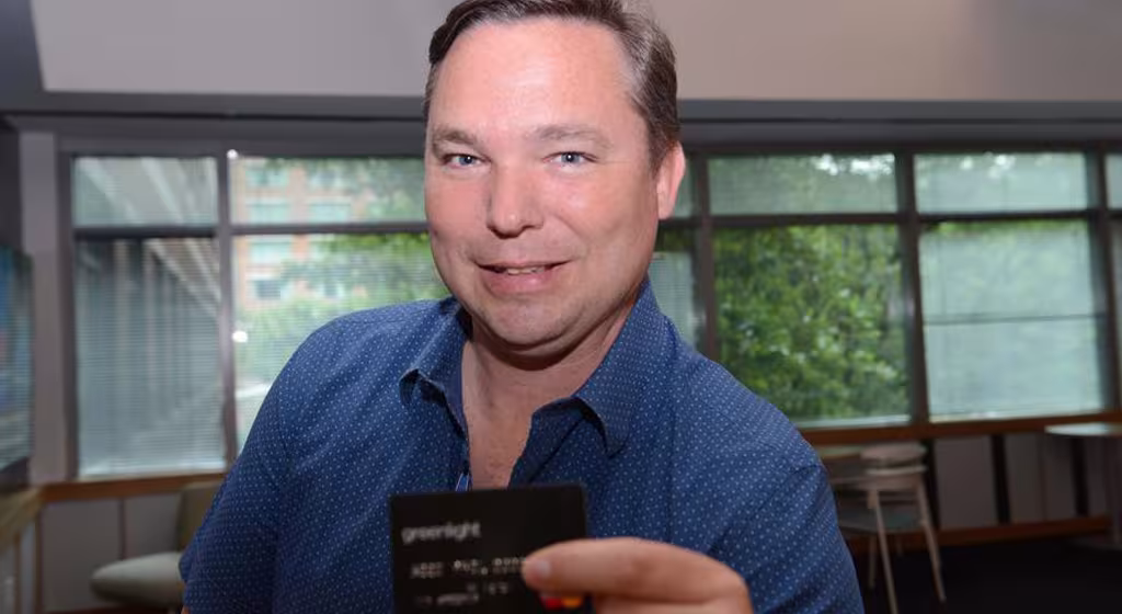 Person holding a payment card toward the camera in an office setting with large windows in the background.